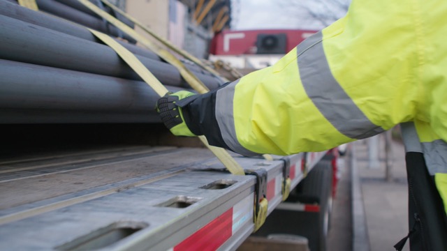 Photo of JLE Professional Flatbed Driver in high visibility jacket checking securement straps for steel tubing flatbed load