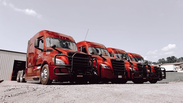 Photo of four red JLE Freightliner trucks outside a warehouse